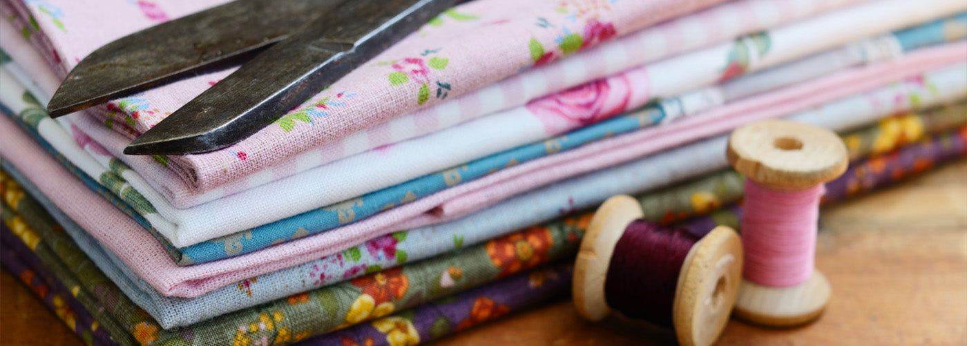 stack of fabrics with different patterns and designs with a pair of scissors on top and sewing thread to the side